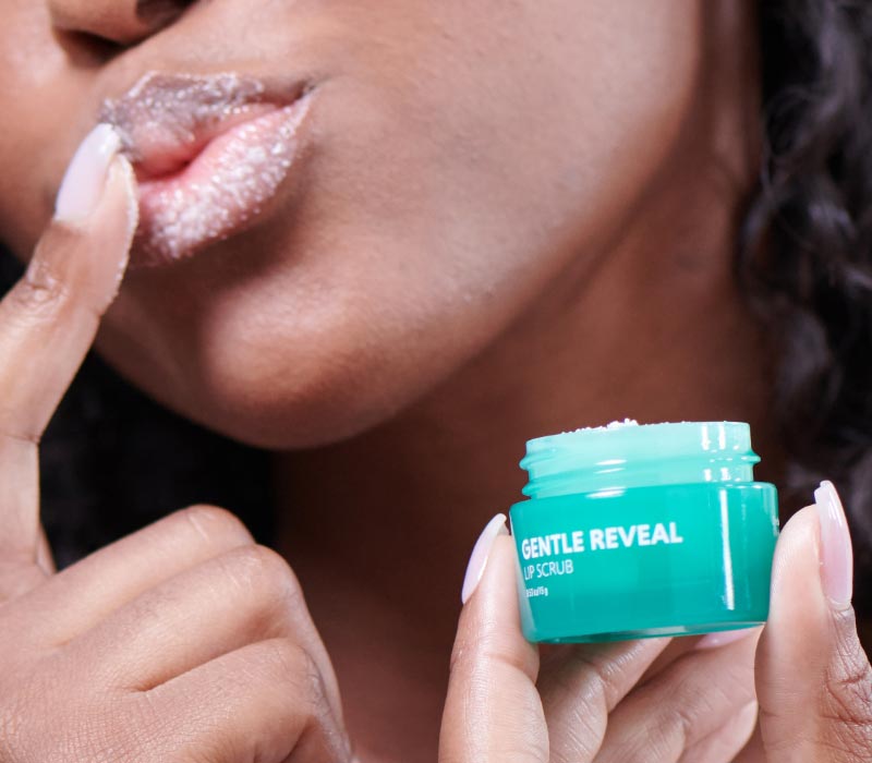 Woman putting Neora’s Hot List product, Gentle Reveal Lip Scrub, on her lips with her fingers